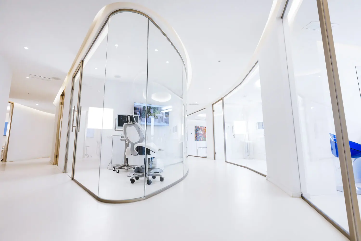 Pasillo de una clínica dental con cabinas de cristal curvado y luz natural